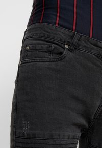 Μαύρα τζιν παντελόνια με κοντινή λήψη μιας μπροστινής τσέπης, με ορατές λεπτομέρειες ραφής και φθαρμένη υφή στην περιοχή του γόνατου.