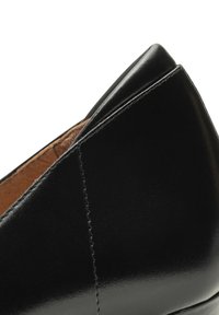 Scarpa in pelle nera con un design elegante, texture liscia, punta appuntita e sottili dettagli di cucitura lungo la cucitura.