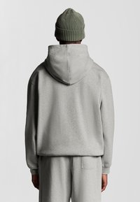 Grå oversized hoodie med snoretræk i hætten, blød tekstur og kengurulomme. Bæres med matchende grå bukser og en grøn ribbet beanie.