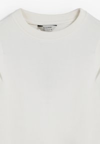 Sudadera blanca con cuello redondo acanalado, textura suave y detalles de costura sutiles cerca de los hombros. Etiqueta visible en el interior.