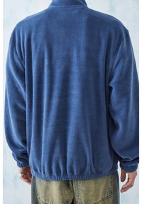 Blå fleecejacka med hög krage, elastisk nederkant och långa ärmar, med en mjuk textur och en avslappnad passform.