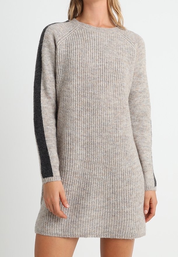 Femme portant une robe-pull tricotée à manches longues et longueur genoux en gris clair avec une bande grise foncée le long de la partie extérieure des manches.