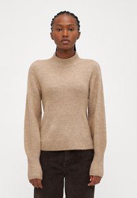 Maglione beige lavorato a maglia con collo alto, texture a coste e maniche lunghe, abbinato a pantaloni in corduroy scuri.