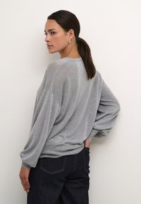 Jasnoszary, oversize sweter z długimi rękawami, prążkowanym wykończeniem i teksturowanym materiałem; zestawiony z ciemnogranatowymi dżinsami.