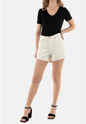 Shorts de mezclilla blanca con cintura alta, con un cierre de botón en el frente y bolsillos. Combinados con una blusa negra ajustada de escote en V y tacones negros.