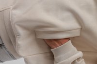 Χέρι στην τσέπη ενός μπεζ σακακιού με ριμπ μανσέτα, που δείχνει την υφή του υφάσματος και το σχεδιασμό της τσέπης σε κοντινό πλάνο.