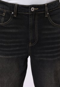 Jeans de mezclilla negra con costuras amarillas, que cuentan con un cierre de cremallera y botón, dos bolsillos frontales y una ligera textura desgastada en la tela.