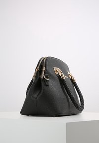 Zwarte handtas met een gestructureerde vorm, dubbele ritssluiting, gevlochten handvatten en accenten in goudkleurig metaaldraad.