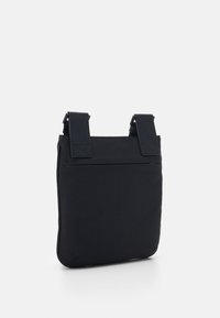 Svart axelväska i slät textil, utrustad med två justerbara remmar och en minimalistisk design med en dragkedjeficka på baksidan.