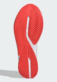 Suela de zapato atlético blanca con una suela exterior de goma roja texturizada, que presenta surcos y crestas distintivas para proporcionar tracción y soporte.
