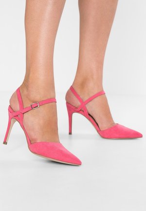 Chaussures à talons hauts en suede rose, avec des pointes effilées, dotées d'une bride à la cheville et d'un design entrecroisé. Hauteur du talon d'environ 10 cm.