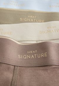 Négy szövetpánt világoskék, bézs, olajzöld és barna színben, mindegyiken arany színnel a derékrészen a "NEXT SIGNATURE" felirat van gravírozva.