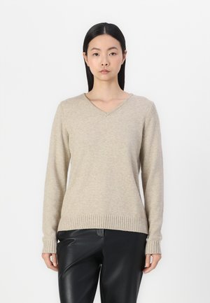 Beige strikket sweater med V-hals, ribbet kant og manchetter. Har lange ærmer og en blød tekstur, parret med sorte læderbukser.