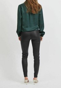 Zelená saténová blůza s knoflíkovými manžetami v kombinaci s černými legínami z umělé kůže. Má slim fit střih a vysoké podpatky.