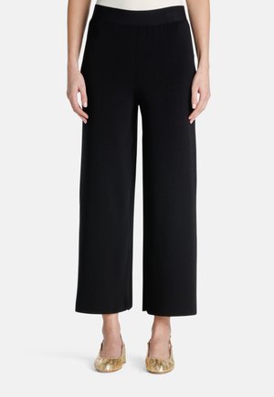 Wijdvallende zwarte broek met een soepele textuur en een elastische tailleband, gecombineerd met gouden slingback schoenen met een reptielachtige patroon.
