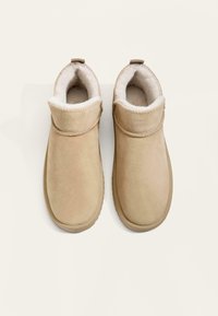 Beige mockalstövlar med mjukt, vitt pälsfoder och rund tå. Har en vikbar krage och gummisulor för bra grepp.