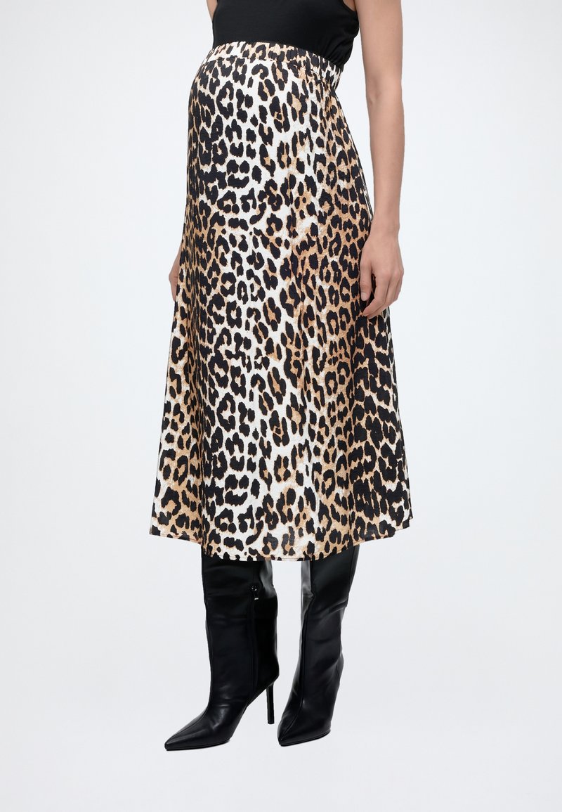 Γυναίκα που φοράει μίντι φούστα με λεοπάρ σχέδιο συνδυασμένη με μαύρες μπότες με ψηλό τακούνι έως το γόνατο, εμφανιζόμενη από τη μέση έως τα πόδια σε λευκό φόντο.