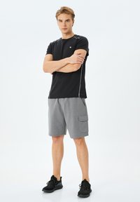 Czarna sportowa koszulka z krótkim rękawem i szarym paskiem. Szare spodenki z kieszonką z boku. Czarne trampki z teksturowanymi sznurówkami.