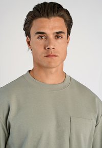 Ljusgrön crewneck sweatshirt med en ficka på vänster bröst, tillverkad av mjukt tyg, med en avslappnad passform och ribbade ärmslut.