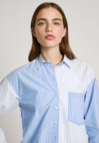 Blauw-wit gestreepte overhemden met knopen en een patch zak. Heeft een kraag en een relaxte pasvorm met verticale strepen in verschillende breedtes.