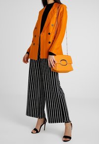 Oranžový pruhovaný dvouřadý blazer, černý upnutý top, široké kalhoty s černobílými pruhy, černé vysoké sandály a oranžová kabelka.