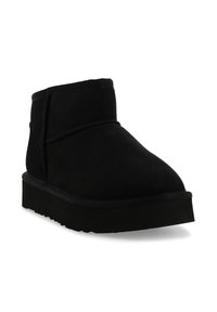 Stivale alla caviglia in suede nero con suola in gomma piatta e dettagli di cucitura minimi, visto da un angolo leggero su uno sfondo bianco.