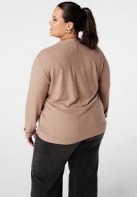 Lichtbruine trui met lange mouwen, in een ontspannen fit en een zachte textuur; gecombineerd met donkergrijze, losse broek.