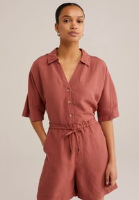 Rostfärgad kort jumpsuit med krage, framknappar och elastisk midja. Har uppvikta korta ärmar och en strukturerad tyg.