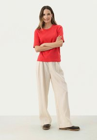 Haut rouge à manches courtes avec un col rond, associé à un pantalon large beige clair et des chaussures sombres à semelles épaisses.