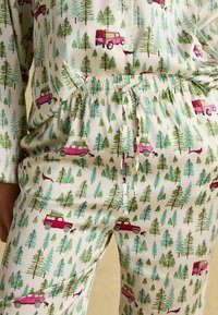 Pajama set featuring a light cream fabric with a repeating pattern of green trees and pink vintage trucks. Elastic waistband with a drawstring.