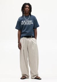 Námorně modré oversized tričko s bílým textem, spárované se světle šedými širokými kalhotami a černými žabkami, doplněné o stříbrný řetízek.