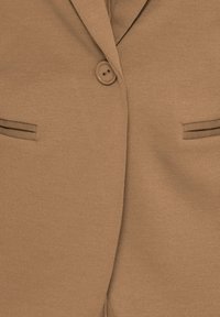 Blazer marron avec une fermeture à un bouton, col à revers cranté et deux poches horizontales fendues à l'avant.
