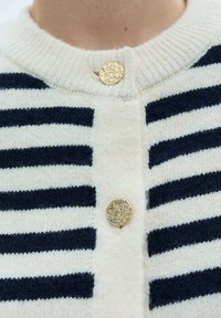 Buttoned cardigan with white and navy horizontal stripes. Made of soft knit material, featuring a round neckline and ornate gold buttons.