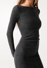 Graues langärmeliges Kleid aus einem weichen, strukturierten Stoff. Figurbetonter Schnitt mit U-Boot-Ausschnitt und gerafftem Detail in der Taille.