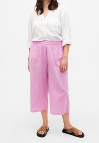 Culotte rosa chiaro con elastico in vita, realizzati in un tessuto testurizzato. Abbinati a una camicia bianca con bottoni e sandali marroni.