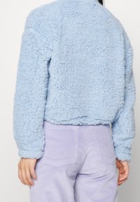 Ljusblått fluffigt jacka med en texturerad, fluffig material och en kort design, kombinerad med lavendelvävda byxor.