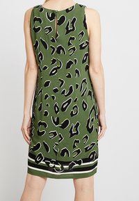 Vestido verde sin mangas con estampado de leopardo en blanco y negro, que presenta una espalda con abertura en forma de llave y un detalle de dobladillo a rayas en la parte inferior.