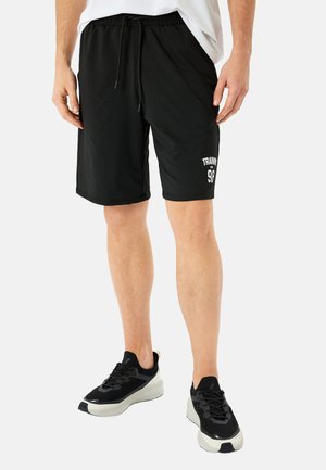 Pantalones cortos de entrenamiento negros con cintura elástica y cordón. Presenta el texto "ENTRENAMIENTO" y el número "98". Se lleva con zapatos deportivos negros.