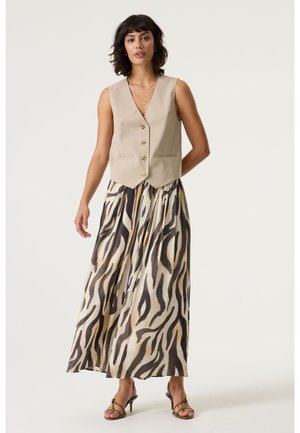 Veste beige sans manches à boutons associée à une jupe longue et fluide avec un imprimé zèbre noir et marron. Tissu texturé avec deux poches.