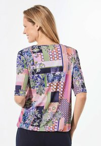 Haut à manches courtes coloré présentant un mélange de motifs en rose, bleu et vert avec des designs floraux et géométriques, fabriqué en tissu léger.