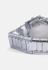Zilveren roestvrijstalen horloge met een schakelbandontwerp. Opvallende kenmerken zijn een gladde, glanzende afwerking en drie metalen knoppen aan de zijkant.
