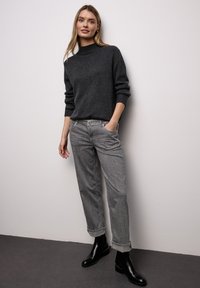 Sweter z golfem z węgla drzewnego, jasnoszare spodnie w wzory oraz czarne botki za kostkę. Prosty fason o luźnym kroju z podwiniętymi mankietami.