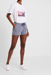 White T-shirt with a printed design, gray drawstring shorts, and white sneakers. The shorts feature side pockets and a textured fabric.