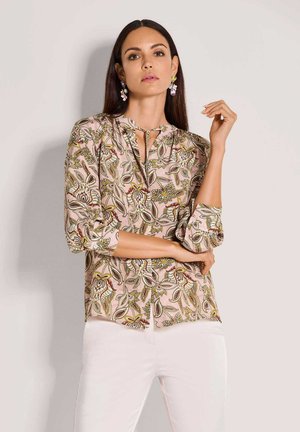 Bluse mit Blumenmuster in Pink und Grün, 3/4-Ärmeln, Schlüssellochausschnitt und weichem Stoff. Kombiniert mit weißen, schlank geschnittenen Hosen.