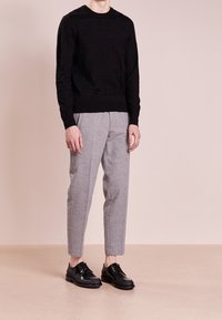 Musta teksturoitu neulepusero, vaaleanharmaat räätälöidyt housut ja mustat nauhakenkäiset kengät. Asu on istuva ja siinä on hienovaraiset kuviot.