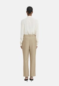 Világos krémszínű blúz hosszú ujjakkal és hátul pliszírozott részletekkel, világos bézs, magas derekú nadrággal párosítva, sima textúrával és rugalmas derékkal.