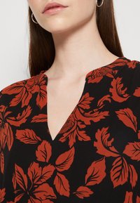 Blusa negra con escote en V, con un patrón floral de color óxido. La tela parece ligera y de textura suave.