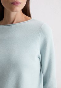 Hellblauer Pullover mit glatter Textur, Bootsausschnitt und langen Ärmeln. Der Stoff wirkt weich und leicht flauschig.