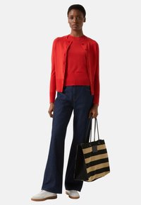 Czerwony kardigan i bluzka zestawione z ciemnoniebieskimi jeansami o szerokich nogawkach. Torba na ramię w czarno-beżowe paski. Białe trampki z brązowymi podeszwami.