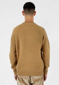 Maglione beige lavorato a maglia con una texture a coste, colletto rotondo e maniche raglan, caratterizzato da un orlo e polsini aderenti.